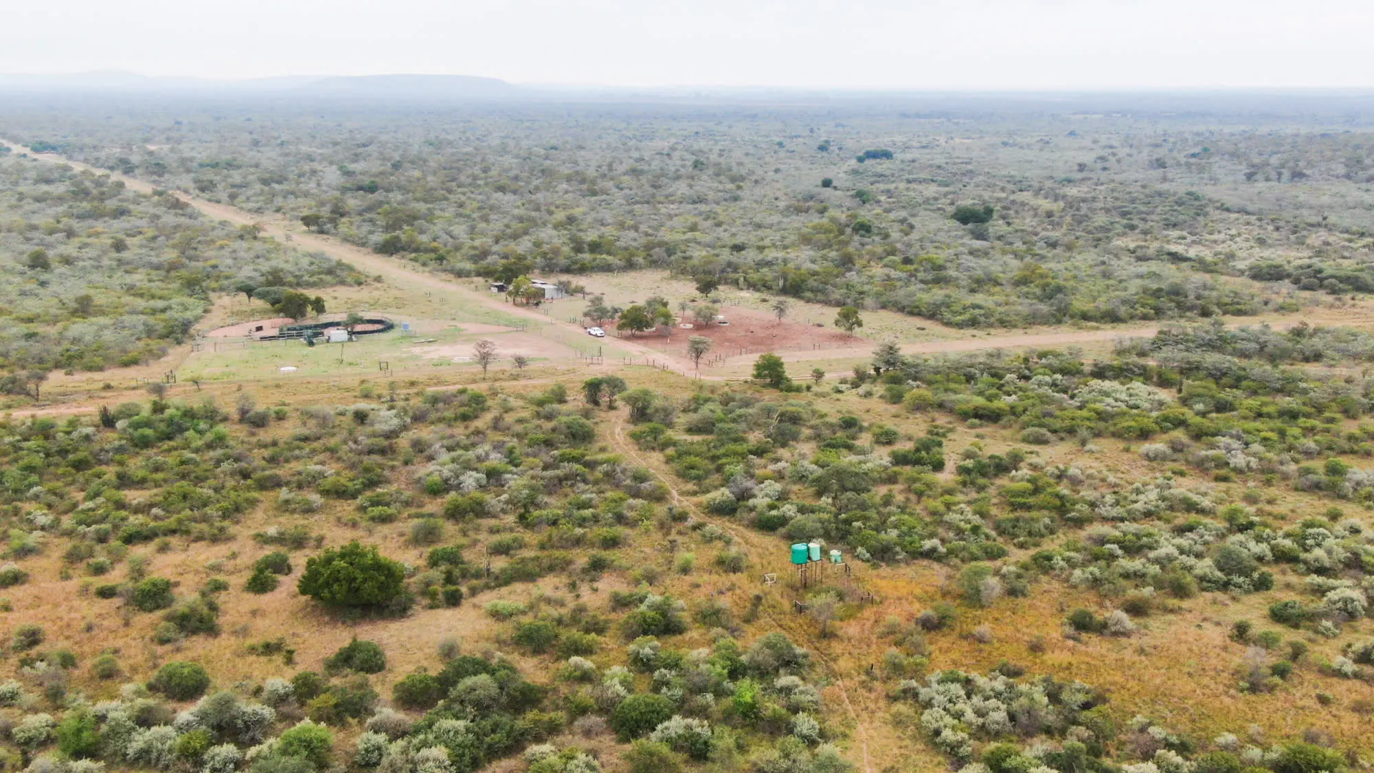 Lugfoto van die trustplaas: bosveld, grondpaaie, 'n skoon werf en groen watertenks
