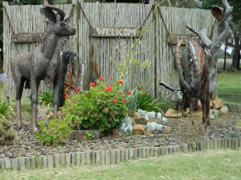 Twee koedoebeelde en 'n Welkom-bord agter 'n bedding rooi blomme