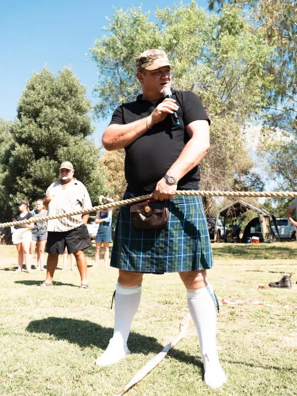 'n Familielid in 'n blou-en-groen tartan-kilt lei die toutrek met 'n mikrofoon, April 2023