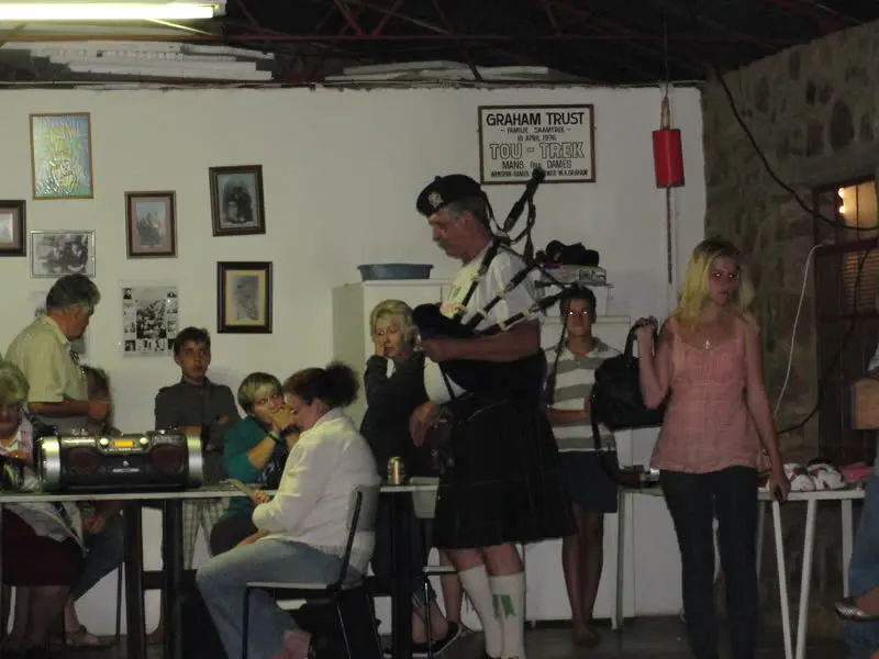 'n Doedelsakspeler in 'n kilt speel in die saal terwyl die familie by lang tafels sit