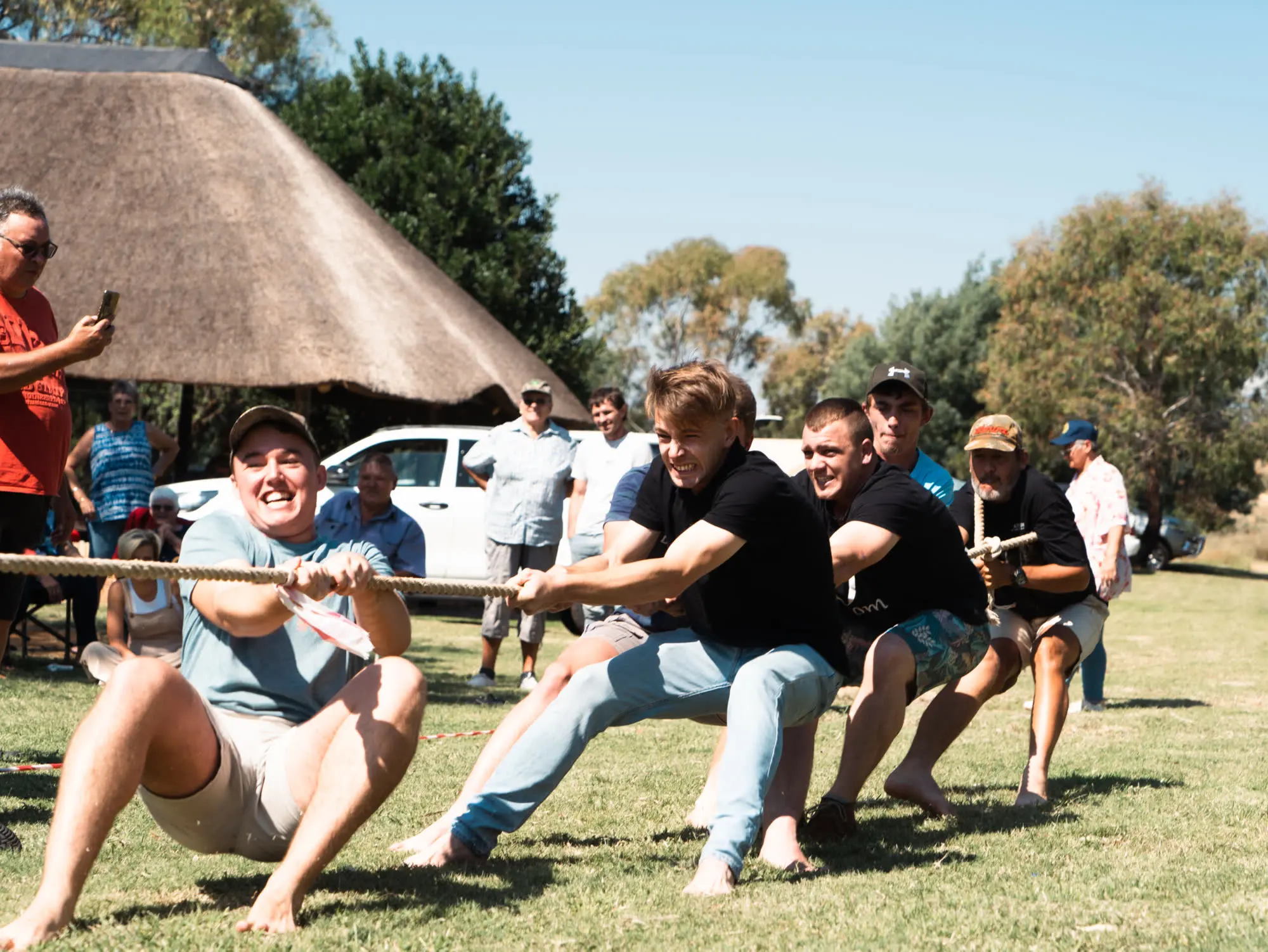 Jong familielede leun agteroor aan die toutrek-tou by die familiefees in April 2023, met die grasdak-lapa agter hulle