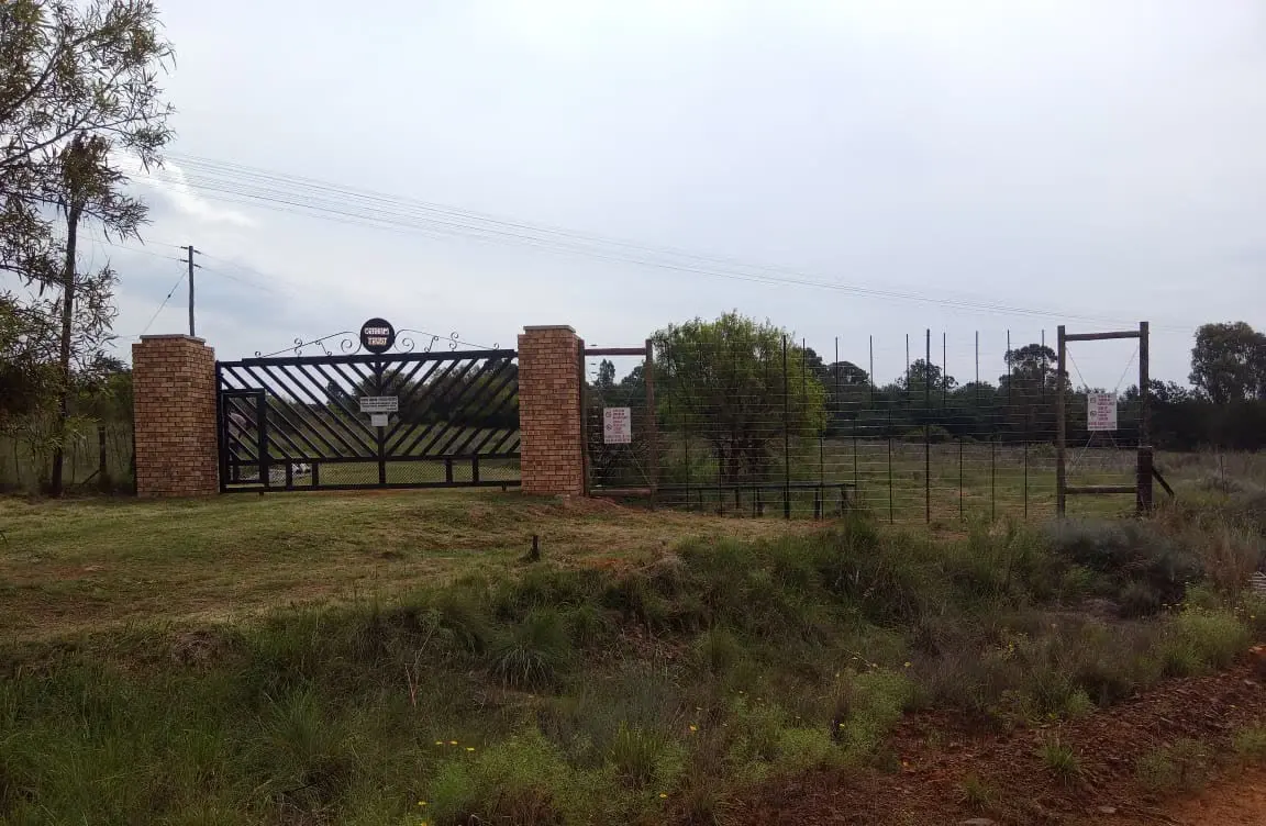 Die Graham Trust-hek tussen twee baksteenpilare, met die plaasheining en veld daaragter